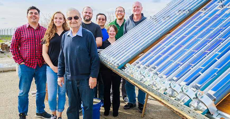 Researchers stand near a large solar collection panel.